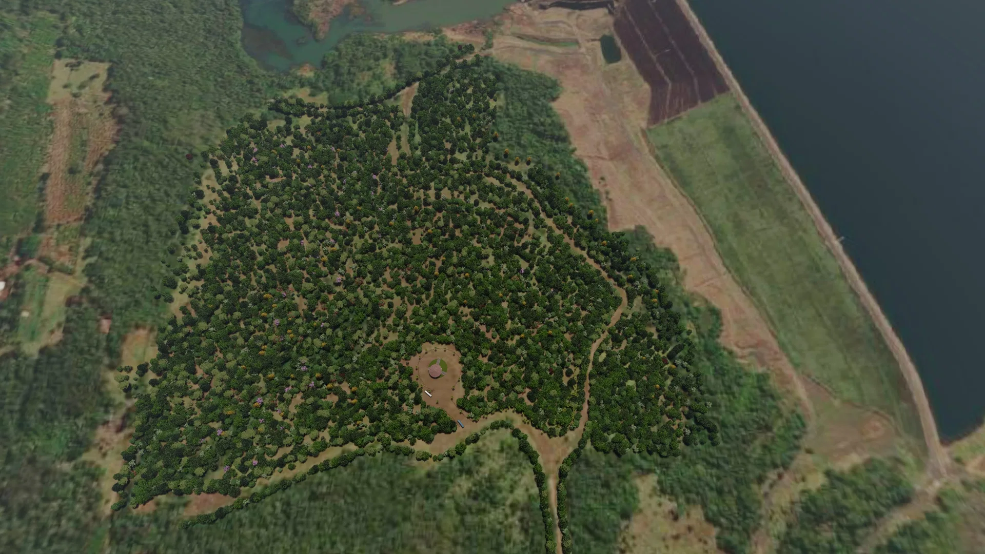 Tomada aérea do platô arborizado com o pavilhão central, cercado por lavouras e amplo espelho d'água ao fundo