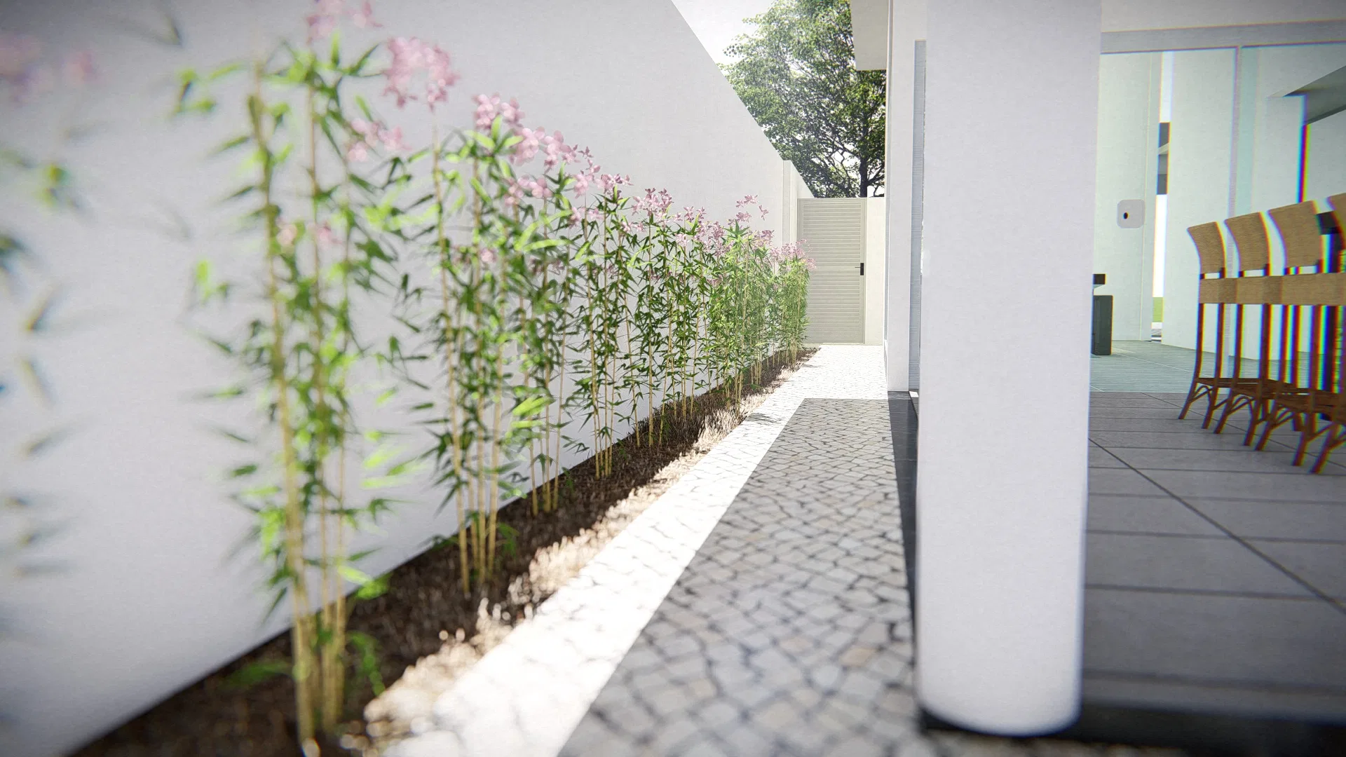 Corredor lateral em pedra portuguesa, com canteiro de bambus e flores rosa junto ao muro branco e área de jantar entrevista à direita