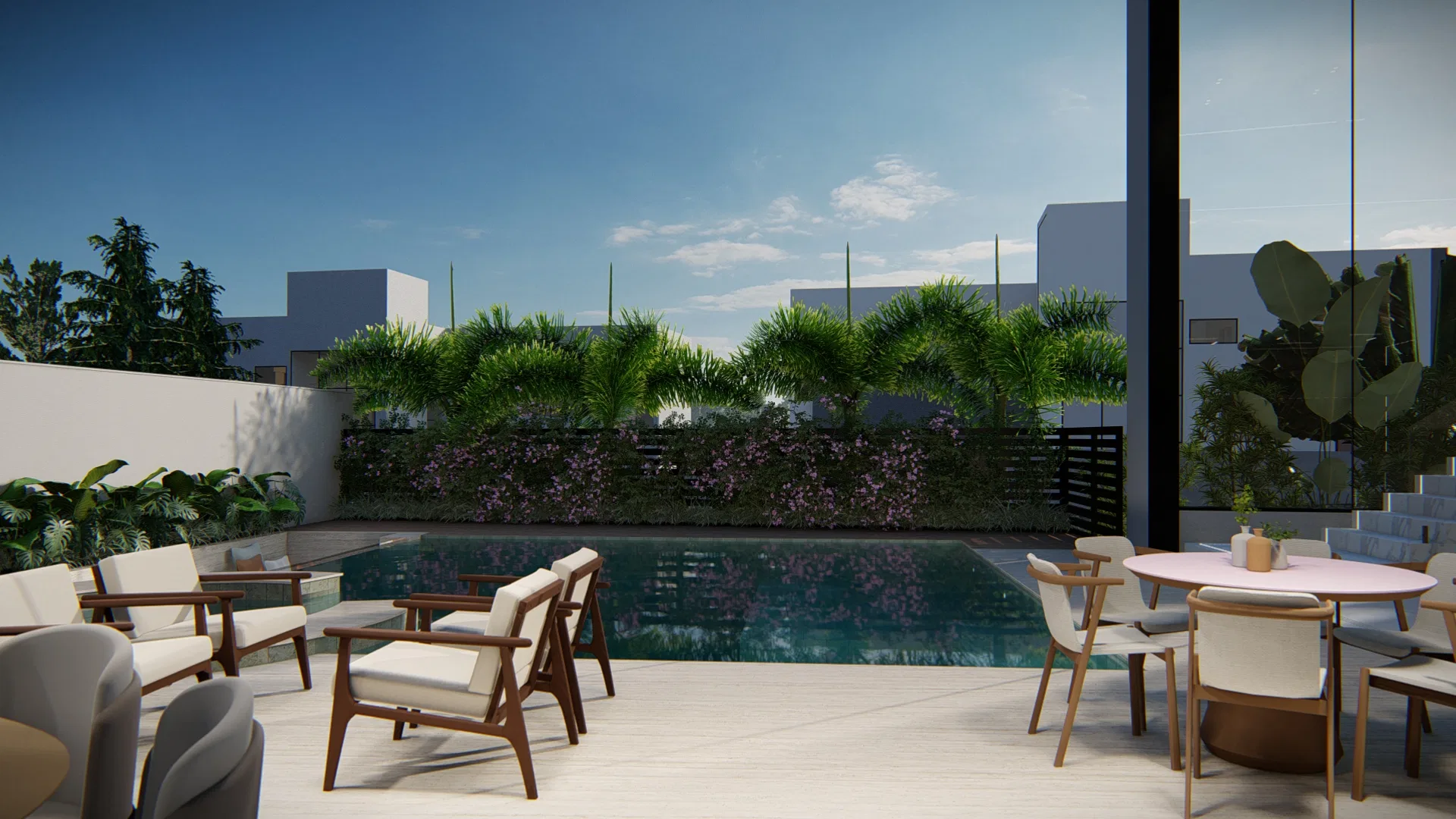 Terraço amplo pavimentado com poltronas de madeira e mesa redonda junto à piscina, tendo ao fundo um muro verde de palmeiras e forração florida.