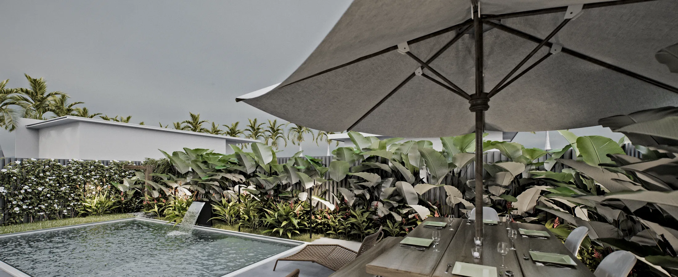 Piscina com lâmina d'água vista de um deque, com guarda-sol cinza sobre mesa posta e cortina densa de folhagem tropical ao fundo.