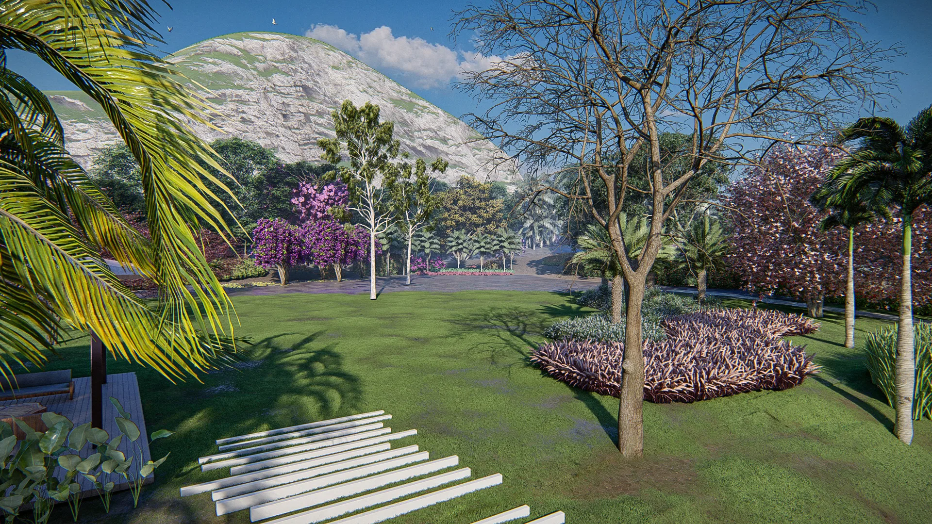 Gramado amplo do jardim com árvores de flores roxas, uma árvore seca em destaque e canteiro de folhagens ao fundo, serra ao horizonte.