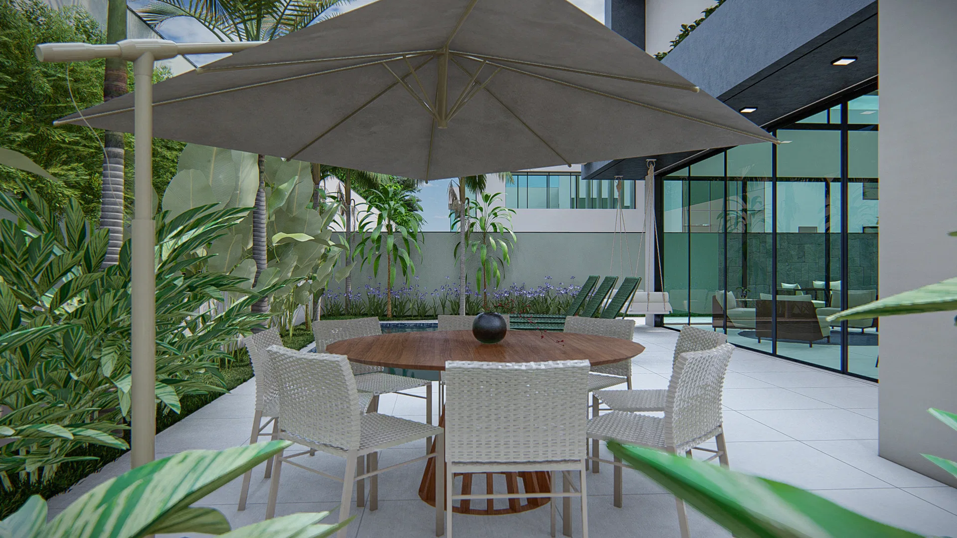 Varanda de refeições com mesa redonda de madeira e cadeiras trançadas claras sob grande guarda-sol, cercada por folhagens e com a piscina ao fundo