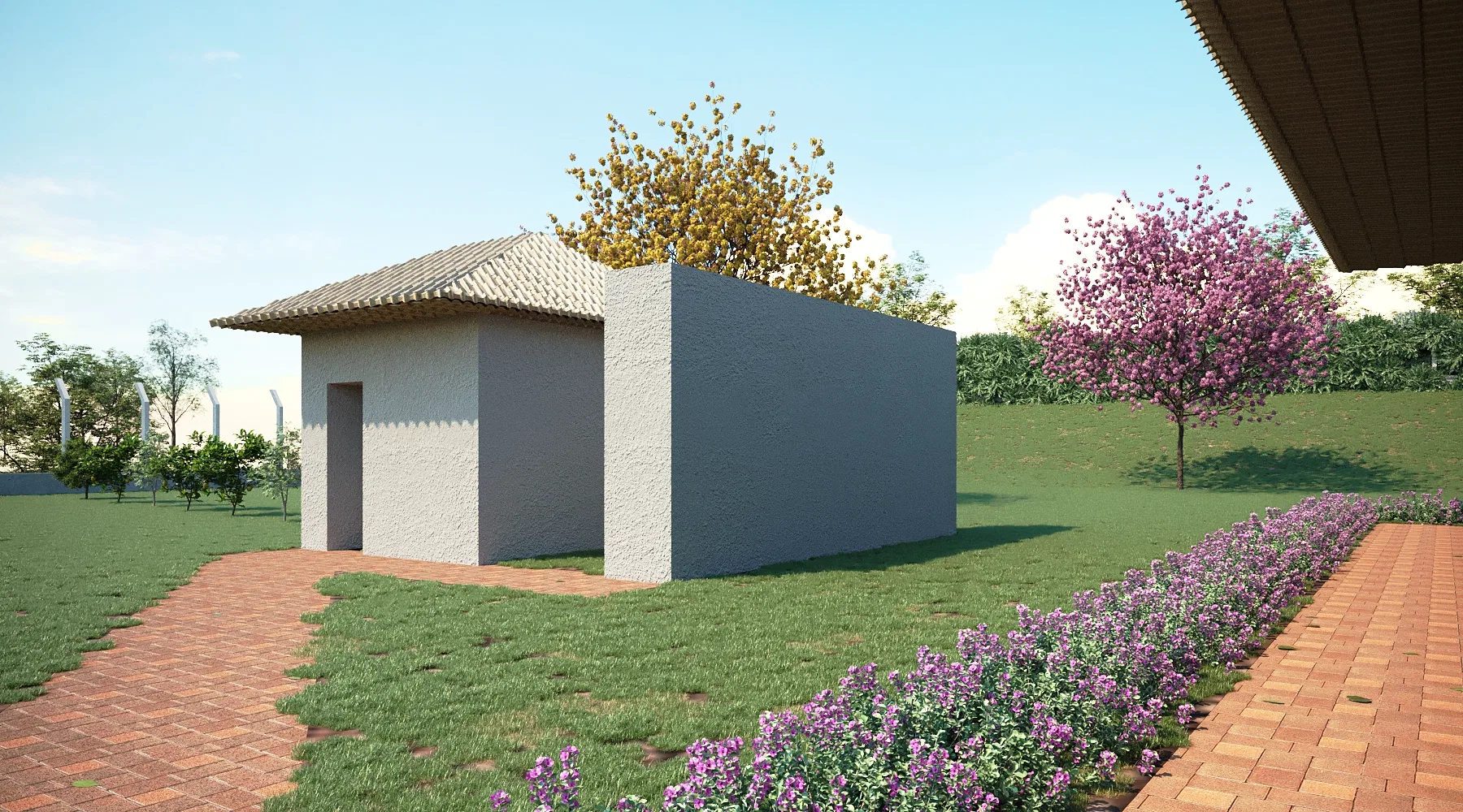 Pequena edificação de apoio com telhado sobre a porta, caminho de tijolinho, canteiro de flores roxas e árvores em flor amarela e rosa.