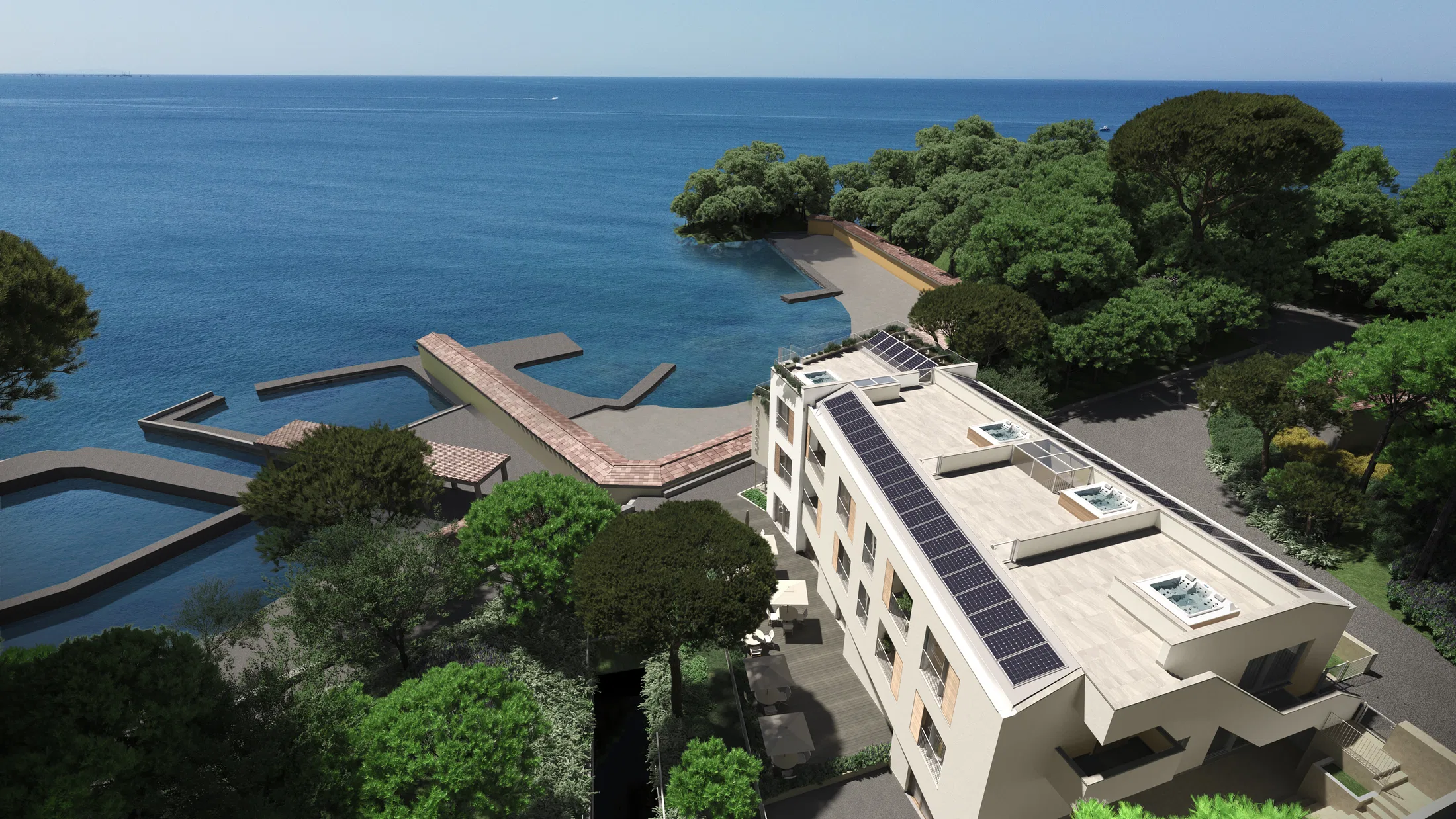 Vista aérea do edifício com placas solares na cobertura, junto a uma enseada rochosa com píeres de madeira avançando sobre o mar azul
