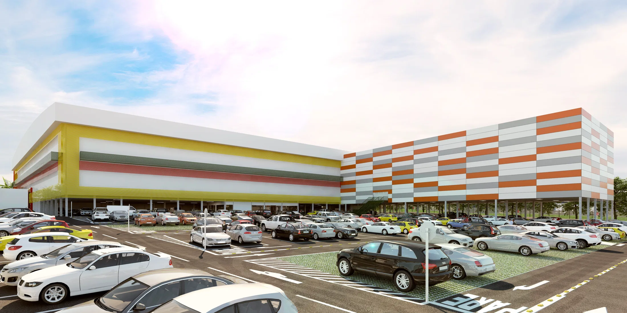 Estacionamento amplo lotado de carros diante do volume baixo do shopping, cuja fachada exibe faixas horizontais coloridas sob céu claro