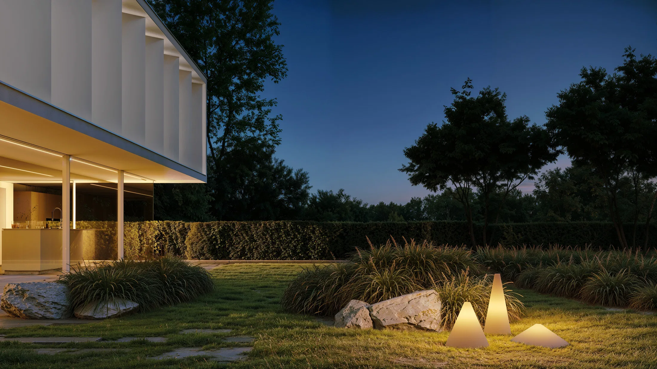 Cena noturna de jardim com as luminárias cônicas acesas sobre o gramado, ao lado de um pavilhão branco com cozinha aberta