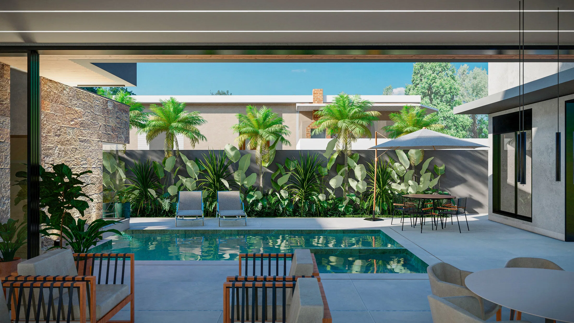 Vista da varanda coberta para a piscina, com mesa de refeições, espreguiçadeiras, palmeiras e folhagens densas junto ao muro escuro e à parede de pedra
