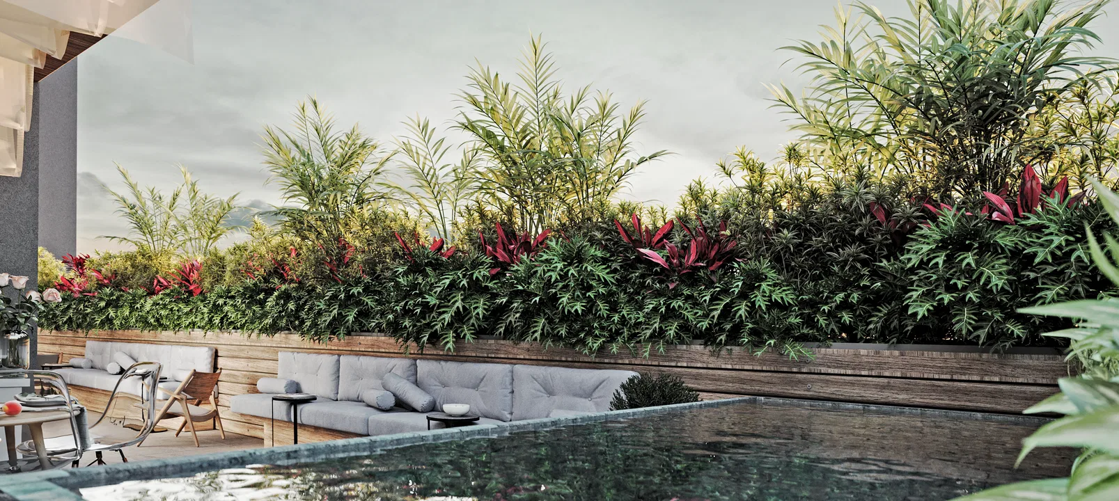 Piscina de borda escura refletindo o céu, contornada por canteiro de madeira com palmeiras, samambaias e cordilines, com sofá baixo e cadeiras de teca ao lado.