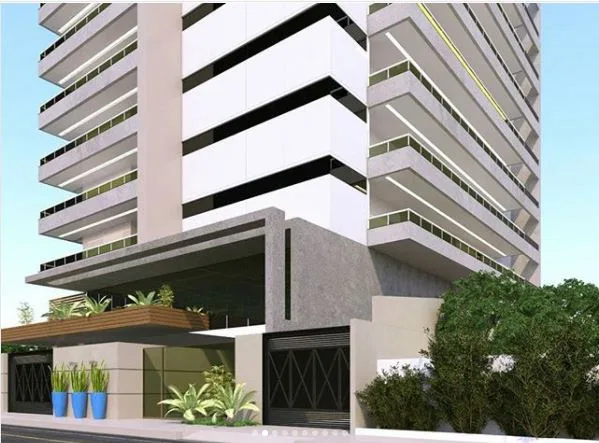 Vista em ângulo do edifício residencial com torre de faixas pretas e brancas ao fundo e vegetação junto ao muro de entrada